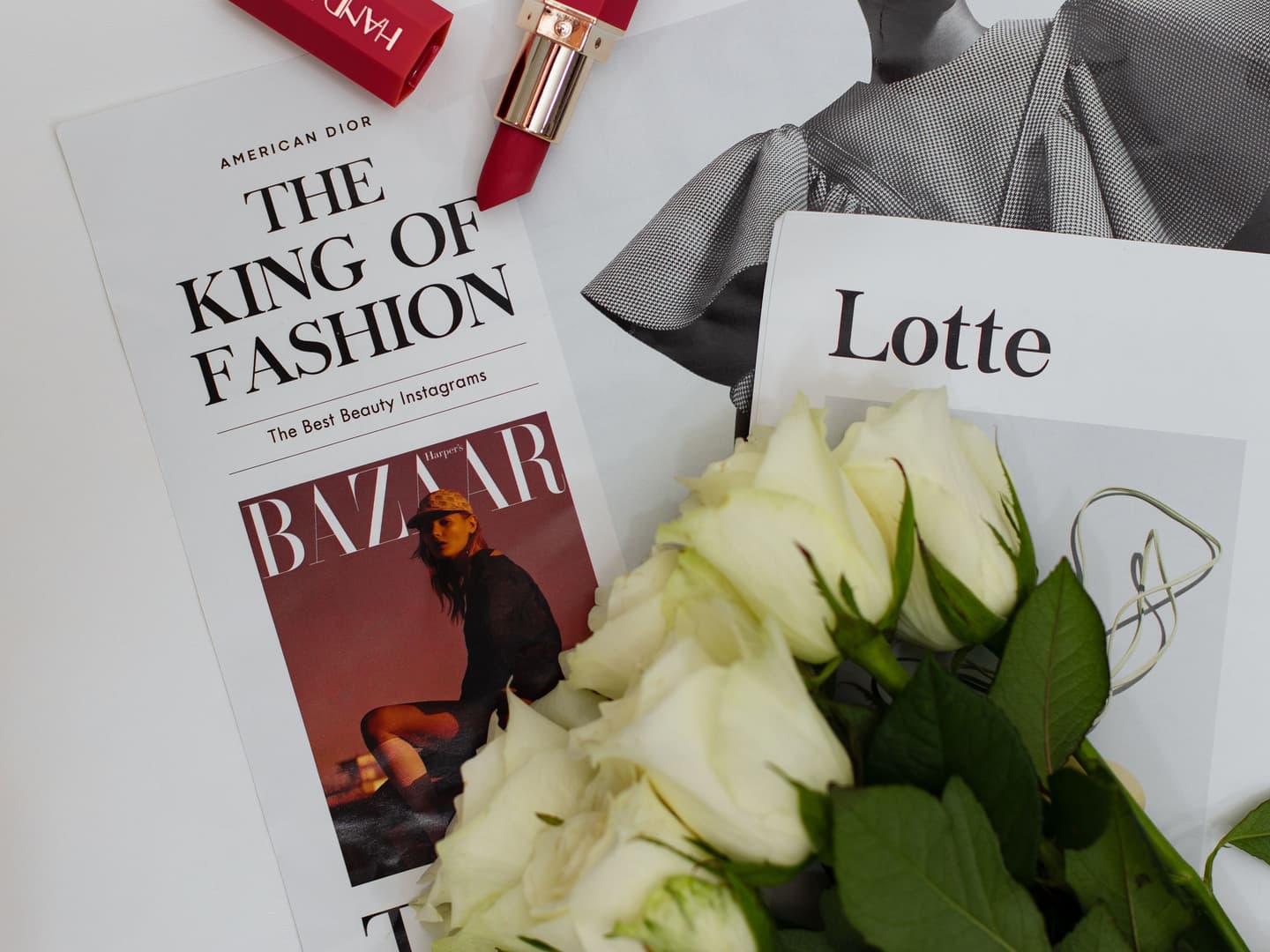 Editorial flat lay with magazines, roses and red lipstick